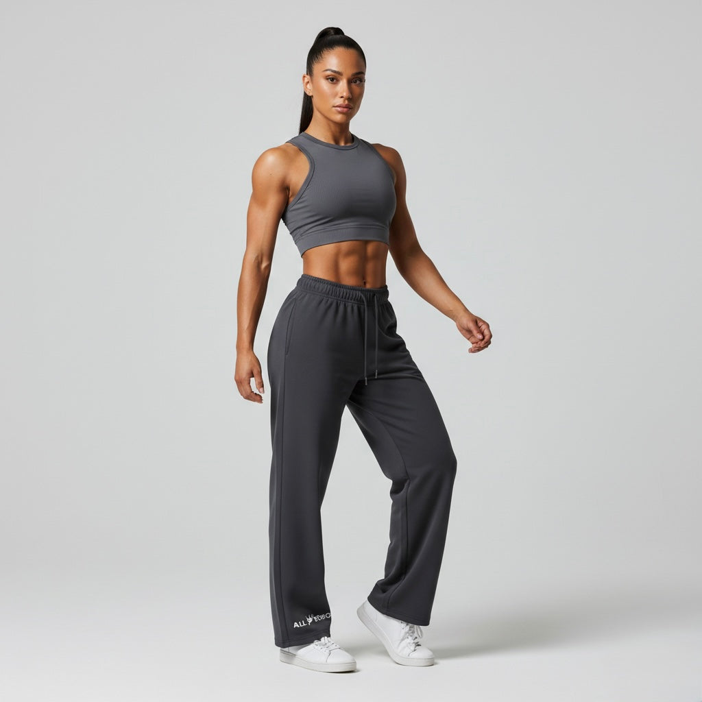 Woman wearing a gray sports bra and black sweatpants with AllBoroughs branding, on a light gray background