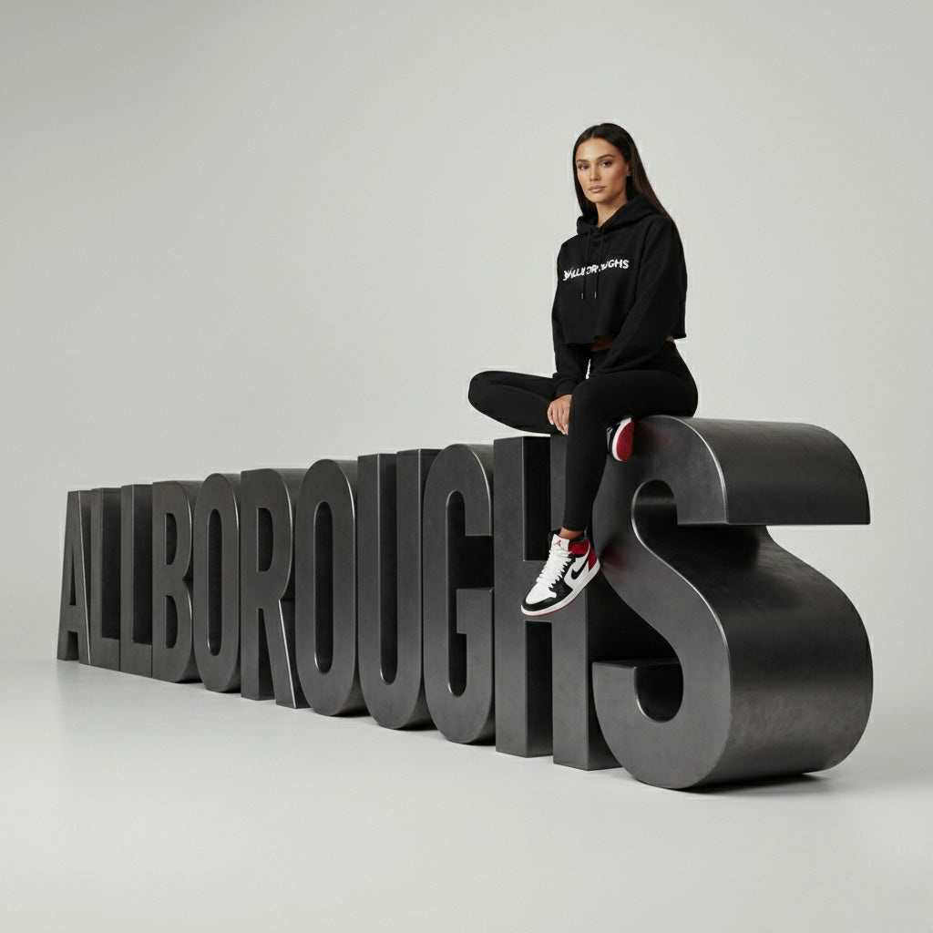 Person sitting on large black letters spelling 'ALLBOROUGHS' against a gray background