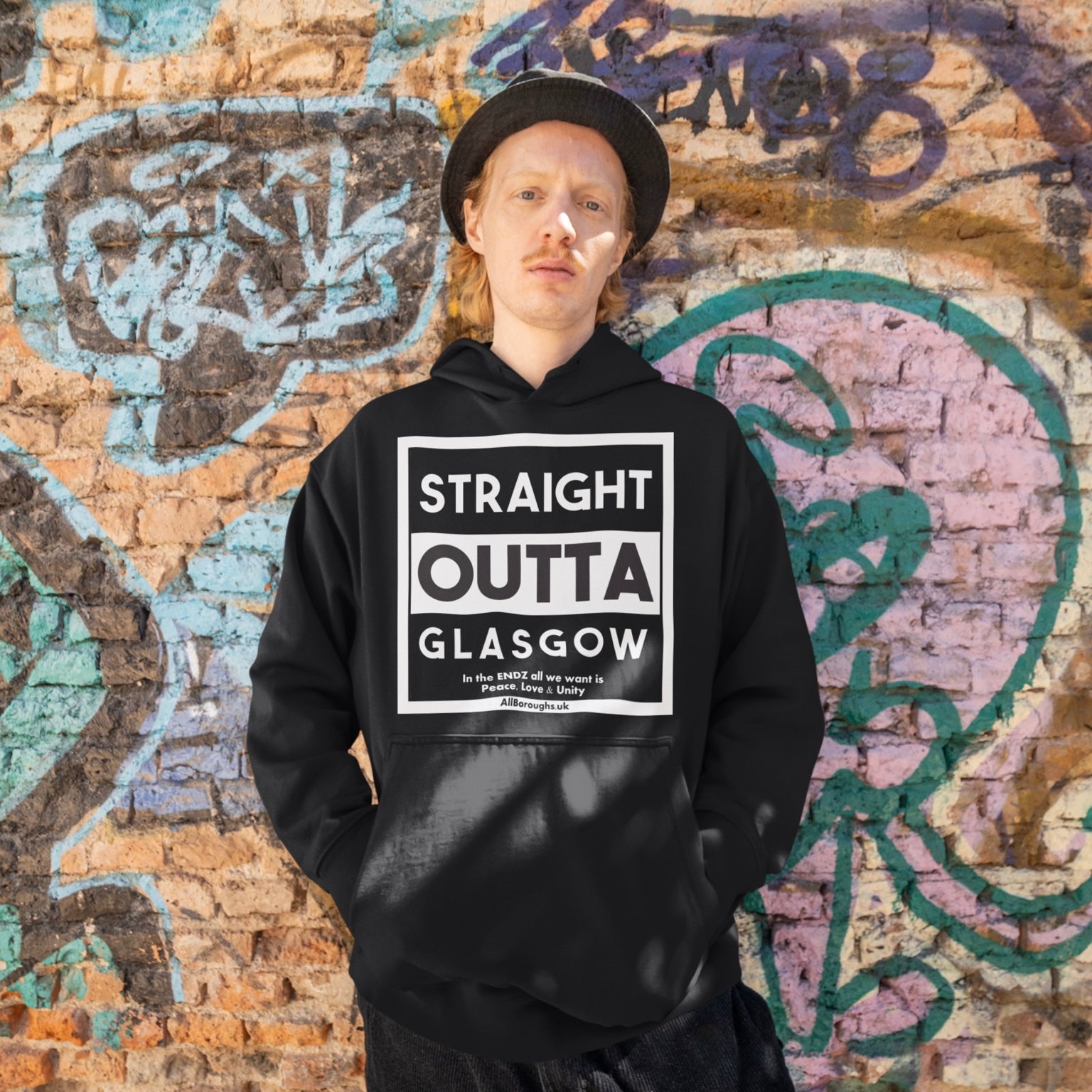 Person wearing a black All Boroughs hoodie with 'Straight Outta Glasgow' text against a graffiti-covered wall.