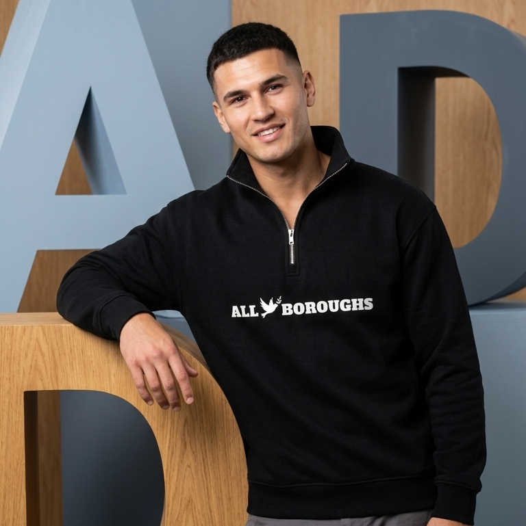 Man wearing a black 'All Boroughs' quarter zip sweatshirt standing in front of large letters