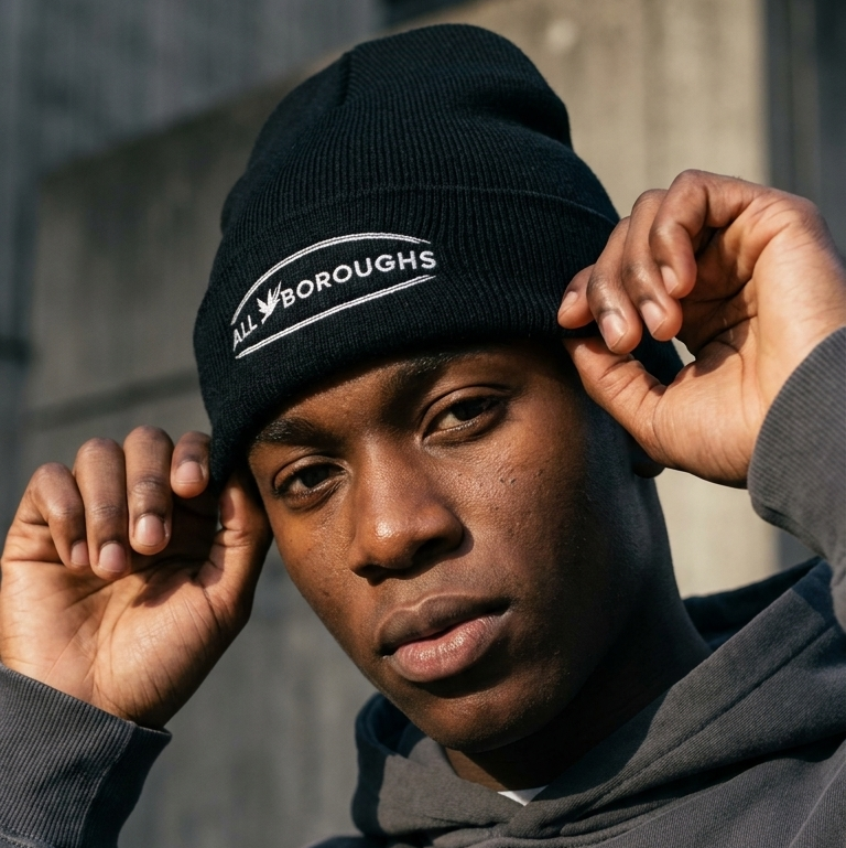 Person wearing a black beanie with 'AllBoroughs' logo against an urban background