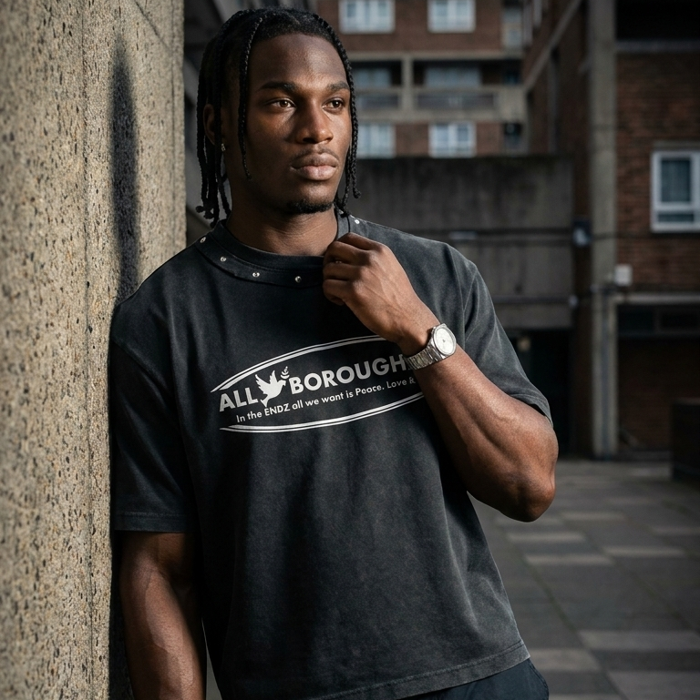 Man wearing a studded 'AllBoroughs' t-shirt leaning against a wall in an urban setting