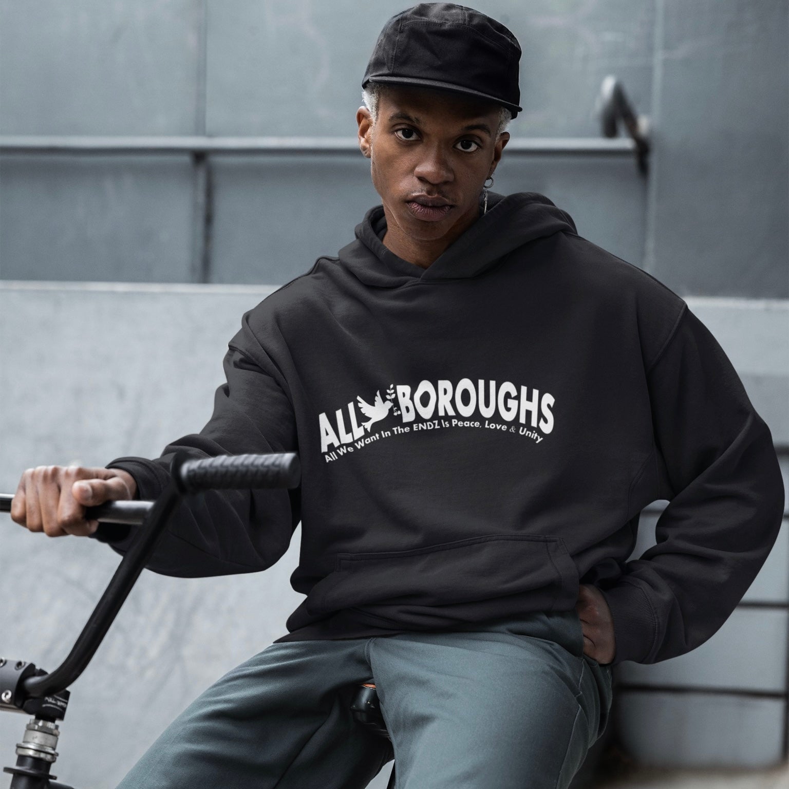 Person wearing a black hoodie with 'All Boroughs' text, sitting on a bench.